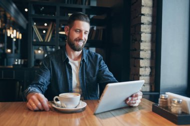 Kafede kahve içme ve tablet bilgisayar kullanarak bir genç adam. Serbest meslek. Çalışma alanı. Öğle Yemeği