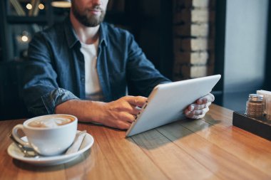 Tablet, kullanma eller erkek ol WiFi bağlanma kapatın. Sadece kafeden çalışma. Genç adam akıllı rahat kıyafet pencere yanında otururken dijital tablet üzerinde çalışan.