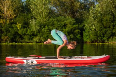 Genç kadın kürek kurulu Sup bir güzel göl veya nehir üzerinde ayağa yoga yapıyorsun. Sağlıklı bir yaşam tarzı kavramı. Spor. Yoga. Hobi