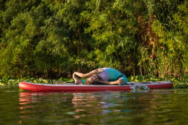 Genç kadın kürek kurulu Sup bir güzel göl veya nehir üzerinde ayağa yoga yapıyorsun. Sağlıklı bir yaşam tarzı kavramı. Spor. Yoga. Hobi