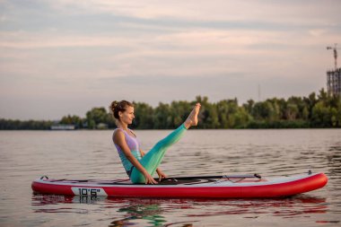 Yoga poz pratik genç kadın kürek gemide otururken. Sup kurulu, etkin yaz dinlenme yapmak yoga egzersiz. Antreman için esneklik ve kas germe.