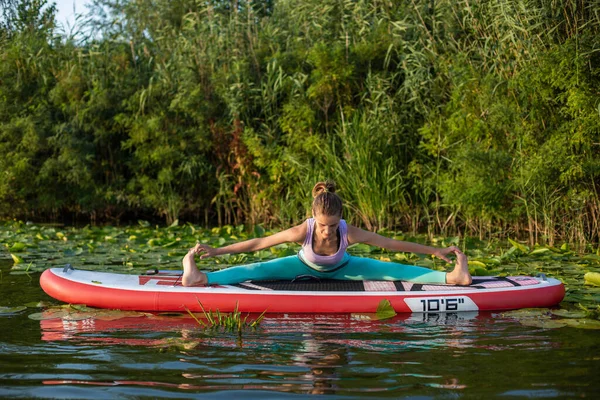 年轻女子正在一个美丽的湖上或河上的划桨板上做瑜伽 健康生活方式的概念 — 图库照片