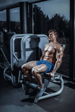 Spor salonundaki bir makinede bacak eklentisi yapan yakışıklı bir adam. Mavi şortlu, gömleksiz yakışıklı bir adam..