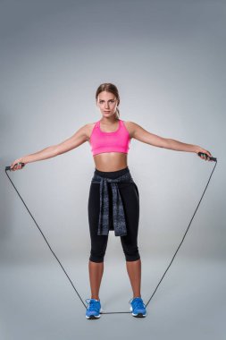 Tam boy görüntü ile gri arka plan üzerinde ip atlama egzersiz yaparak bir güzel fitness kadının. Güzel ince sağlıklı vücut studio poz olan kadın.
