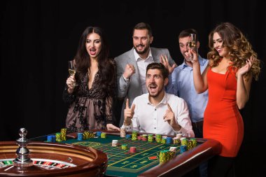 Rulet masasının arkasında bir grup genç siyah arka planda. Kazanan Oyuncu. Parlak duygular