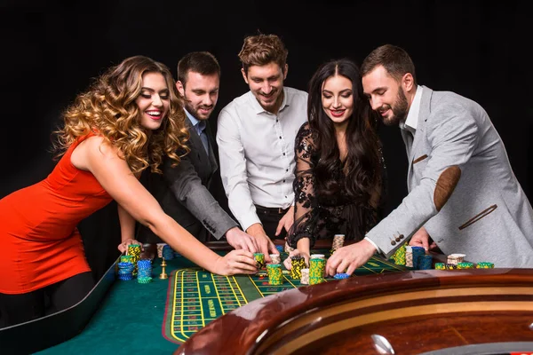 黒い背景にルーレットのテーブルの後ろに若い人たちのグループです 若い人たちがゲームに賭けています — ストック写真