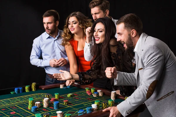 一组年轻人在黑色背景的轮盘赌桌后 情感游戏玩家 — 图库照片