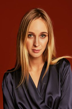 Doğal sarı saçları ve kırmızı arka plan üzerinde poz ile güzel bir moda model portresi. Yakın çekim. Stüdyo vurdu. İpek kokteyl elbisesi