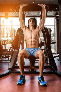 Yük altındaki ellerin gergin kasları. Spor salonunda pazılar için egzersiz yapan bir adam. Simülatördeki kaslara çalış. Spor dergileri, posterler ve web siteleri için fotoğraflar. Güneş parlıyor