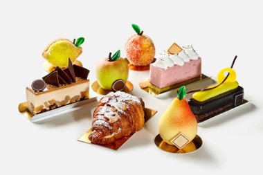 Çeşitli taze kurabiyeler, meyve şekilli pastalar, krema ve çikolatalı pasta dilimleri, pudra şekerli pudra şekerli pudra şekerli poğaça kruvasanı ve beyaz arka planda badem gevreği. Tatlıya düşkünlük