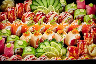 Large set of various Japanese rolls with tuna, salmon and eel packed in cardboard box with pickled ginger, slices of cucumbers and lemon, on black background. Sushi delivery concept clipart