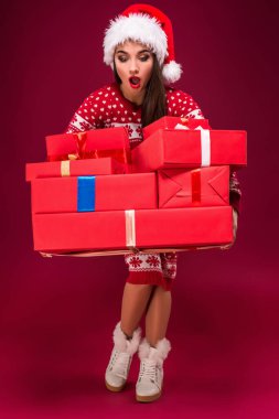 Kırmızı arka planda hediyeler tutan çok güzel bir kadın. Noel Baba şapkalı genç bir kadın kutulara bakıyor. Noel zamanı. İndirim. Dükkanlar. Satılık.