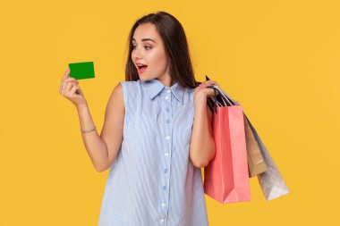 Kredi kartı gösteren ve çok sayıda renkli paket elinde tutan oldukça çekici seksi kız çekici, sarı arka plan üzerinde duran alışveriş için banka kartı kullanmak rahattır. Alışveriş. Satılık