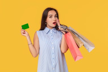 Kredi kartı gösteren ve çok sayıda renkli paket elinde tutan oldukça çekici seksi kız çekici, sarı arka plan üzerinde duran alışveriş için banka kartı kullanmak rahattır. Alışveriş. Satılık
