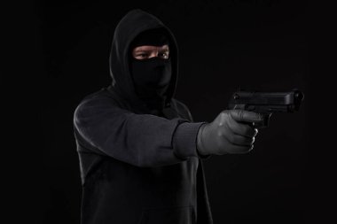 Maskeli ve silahlı soyguncu siyah bir arka planda yan tarafı işaret etti. Silahlı bir adam.
