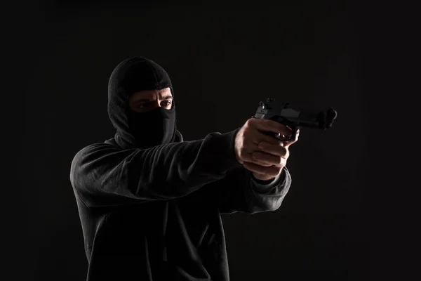 The robber in a mask with a gun pointed to the side on a black background. Man with a gun