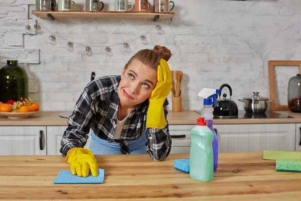 Young woman in protective gloves wipes a table in the kitchen with a rag. Fatigue. Household, cleaning and people concept