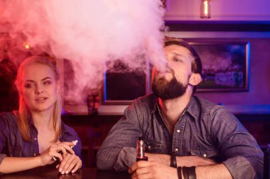 Bir adam ve bir kadın bir vape barda elektronik sigara içiyorlar. Vestiyer.