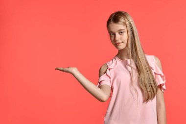 Studio portrait of a gorgeous blonde adolescent with a long hair, in a rosy t-shirt, standing against a pink background in various poses. She expresses different emotions posing right in front of the