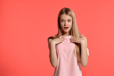 Studio portrait of a gorgeous blonde teenager with a long hair, in a rosy t-shirt, standing against a pink background in various poses. She expresses different emotions posing right in front of the