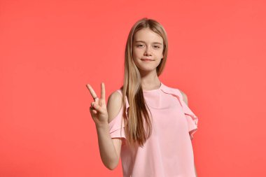 Studio portrait of an attractive blonde adolescent with a long hair, in a rosy t-shirt, standing against a pink background in various poses. She expresses different emotions posing right in front of