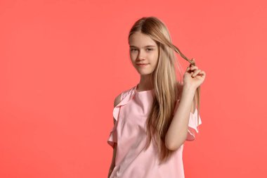 Studio portrait of a beautiful blonde teenage girl with a long hair, in a rosy t-shirt, standing against a pink background in various poses. She expresses different emotions posing right in front of
