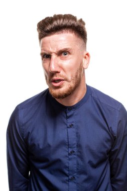 Attractive young bearded man wearing blue shirt is grining and looking mad, isolated over a white background.
