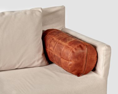 Soft sofa upholstered in light fabric, complemented by handmade bolster pillow made of copper-colored genuine leather with holofiber filling and zipper. Comfortable addition for stylish interior