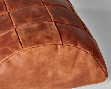 Closeup of hand-stitched semi-cylindrical footstool made from patches of terracotta genuine leather. Stylish comfortable interior accessory