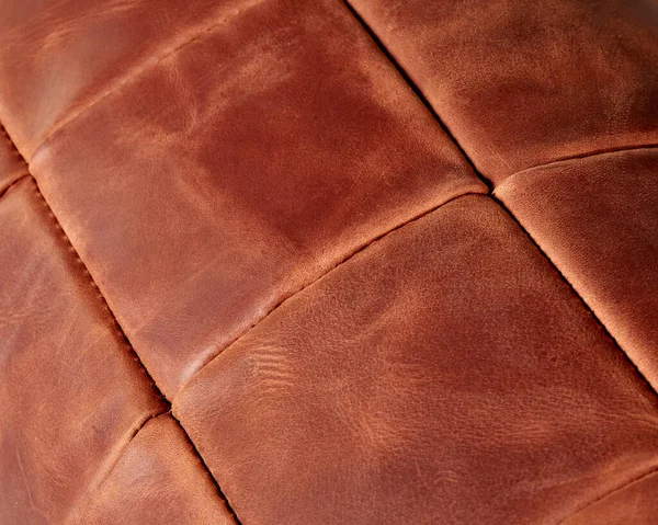 Background of stitched square patches of copper-coloured genuine leather. Handcrafted furniture upholstery. Textured pattern