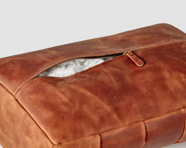 Closeup of hand-stitched copper-colored leather foot cushion with zipper and soft holofiber filling for home and office decor. Comfortable natural handmade interior accessory