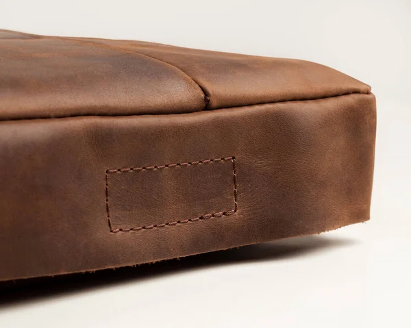 Close-up of upholstered soft seat cushion handmade from genuine brown leather with sewn-on hook-and-loop fastener and finished with neat stitching. Artisanal leather goods