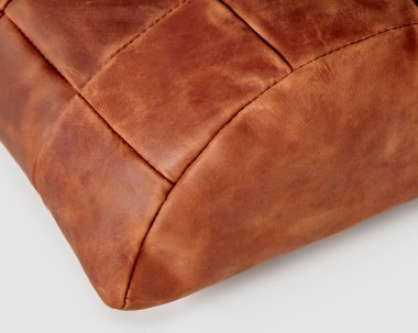 Closeup of half-cylindrical footrest cushion handmade from patches of genuine copper-colored leather. Stylish soft interior accessory, ideal for comfortable work at table