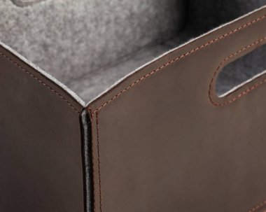Brown genuine leather storage organizer with gray felt lining and slotted handles for carrying. Closeup of box corner neatly stitched for durability. Quality artisanal furnishing accessory