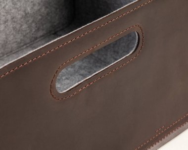Closeup of slotted handle for easy carrying on side of brown leather storage box with gray felt lining and neat stitching. Quality functional handcrafted accessory for home and office interior