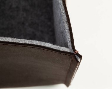 Closeup of corner of brown genuine leather box lined inside with soft gray felt stitched with strong thread. Concept of artisan manufacturing of quality interior decor items