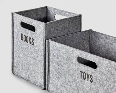 Two handcrafted bins in gray thick felt with handles for comfortable sorting and storage of things. Sides of boxes labeled Toys and Books in black letters. Artisanal interior accessories