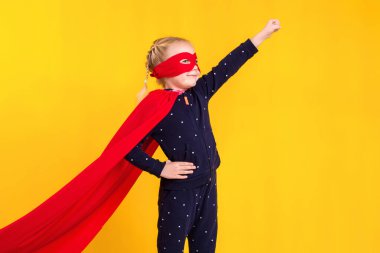 Kırmızı yağmurluk ve sarı arka planda maske takan süper kahraman küçük kız. Stüdyo fotoğrafçılık