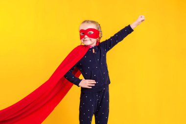 Kırmızı yağmurluk ve sarı arka planda maske takan süper kahraman küçük kız. Stüdyo fotoğrafçılık