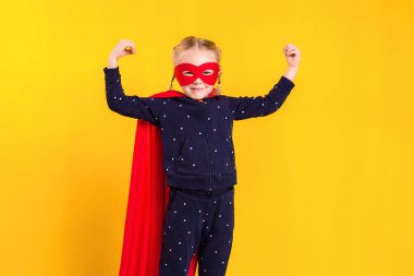 Kırmızı yağmurluk ve sarı arka planda maske takan süper kahraman küçük kız. Stüdyo fotoğrafçılık