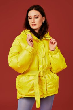 Genç koyu saçlı kız kamera Studio kırmızı zemin üzerine önce poz görüntüsünü kapatın. Sarı ceket giymiş şık kadın moda görüntü