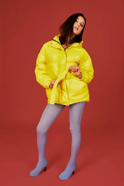 赤い背景のスタジオでカメラの前にポーズをとって暗い髪少女のイメージ 黄色のジャケットを着ているおしゃれな女性のファッション画像 — ストック写真