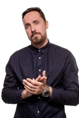 Koyu mavi gömlekli yakışıklı bir adamın portresi, kameraya bakıyor ve ellerini çırpıyor, beyaz bir arkaplanda duruyor. Kendine güvenen adam.