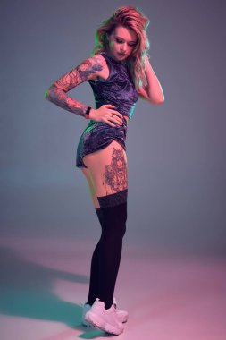 Kadife mavi spor elbiseli ve siyah çoraplı güzel sarışın fitness kızının fotoğrafı stüdyoda baştan çıkarıcı bir şekilde poz veriyor. Pembe ve mavi arka plan. Fitness, spor, twerk, dans