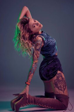 Mavi kadife şort ve kestane rengi süet çizmeler giyen genç, güzel, sarışın kadın, bazı twerk hareketler gösteriyor, baştan çıkarıcı görünüyor..