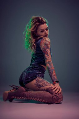 Mavi kadife şort ve kestane rengi süet çizmeler giyen genç, güzel, sarışın kadın, bazı twerk hareketler gösteriyor, baştan çıkarıcı görünüyor..