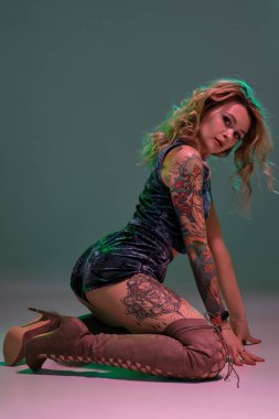 Mavi kadife şort ve kestane rengi süet çizmeler giyen genç, güzel, sarışın kadın, bazı twerk hareketler gösteriyor, baştan çıkarıcı görünüyor..