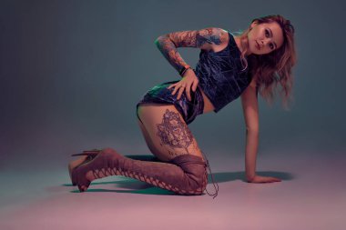 Mavi kadife şort ve kestane rengi süet çizmeler giyen genç, güzel, sarışın kadın, bazı twerk hareketler gösteriyor, baştan çıkarıcı görünüyor..