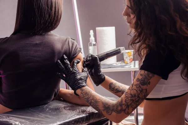 モダンなプロのスタジオで女性の腕に複雑なレタリングとフォントでタトゥーを制作する若い女性のマスタータトゥーアーティスト — ストック写真