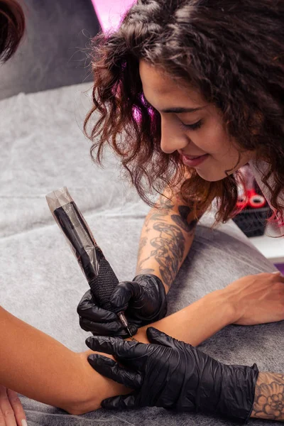 笑顔の若いブルネットタトゥー スタジオでタトゥーを作る 女性の前腕に手紙のアートワークを作成する機械を使用して — ストック写真